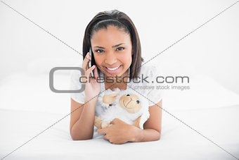 Joyful young dark haired model making phone call while cuddling plush sheep