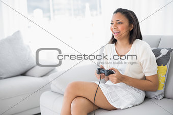 Laughing young dark haired woman in white clothes playing video games