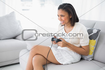 Delighted young dark haired woman in white clothes playing video games