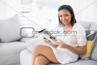 Pleased young dark haired woman in white clothes reading magazines