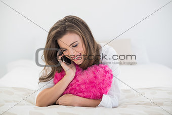 Laughing casual brown haired woman in white pajamas making a phone call