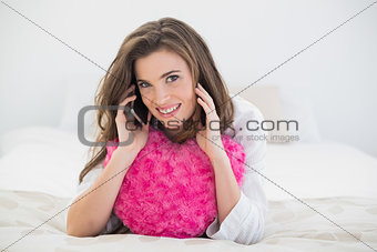 Pleased casual brown haired woman in white pajamas making a phone call