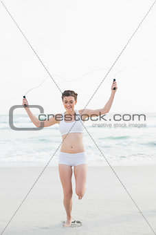 Amused slim brown haired model in white sportswear playing with a skipping rope