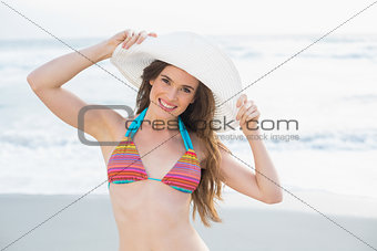Pretty slim brown haired model in coloured bikini wearing a white hat