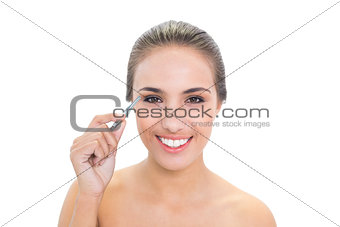 Smiling brunette woman plucking her eyebrows
