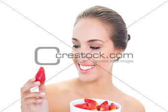 Young brunette woman smiling at a strawberry