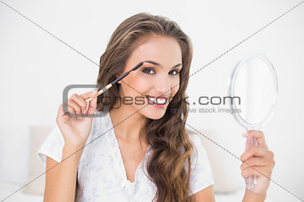 Smiling attractive brunette using eyebrow brush and mirror