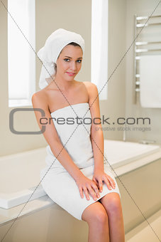 Smiling natural brown haired woman sitting on a bathtub