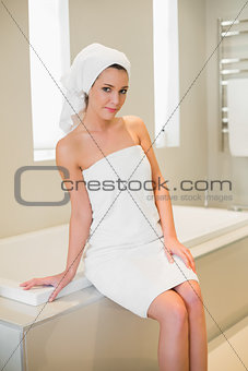 Cheerful natural brown haired woman sitting on a bathtub