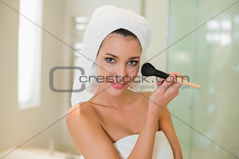 Cute natural brown haired woman applying powder on her face