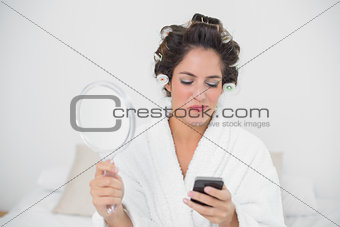 Smiling natural brunette holding mirror and smartphone