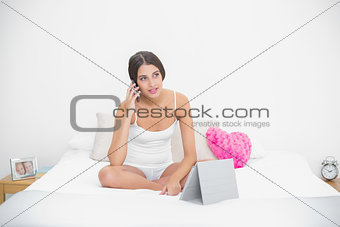 Thoughtful young brown haired model in white pajamas making a phone call