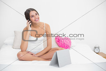 Dreamy young brown haired model in white pajamas making a phone call