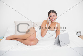Cute young brown haired model in white pajamas making a phone call