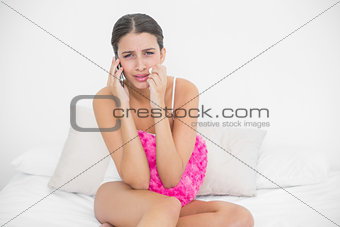 Devastated young brown haired model in white pajamas being dumped by phone