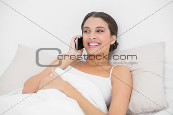 Pensive young brown haired model in white pajamas making a phone call