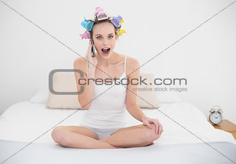 Shocked natural brown haired woman in hair curlers making a phone call