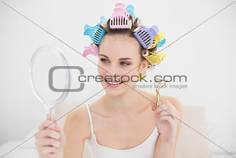 Beautiful natural brown haired woman in hair curlers looking herself in a mirror