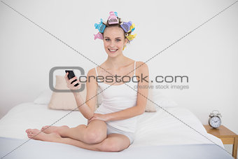 Content natural brown haired woman in hair curlers texting with her mobile phone