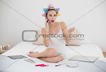 Shocked natural brown haired woman in hair curlers calling with her mobile phone
