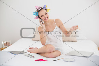 Amused natural brown haired woman in hair curlers calling with her mobile phone