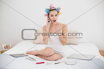 Funny natural brown haired woman in hair curlers making a phone call while applying gloss
