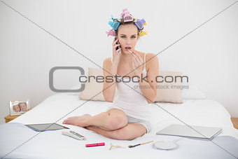 Stern natural brown haired woman in hair curlers applying gloss while being on the phone