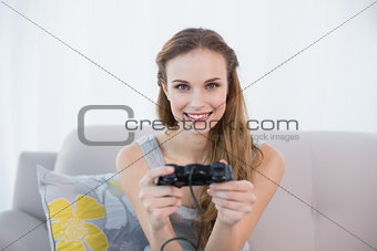 Cheerful young woman sitting on sofa playing video games