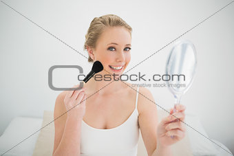 Natural happy blonde holding mirror and using brush