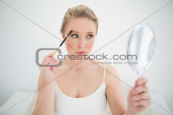 Natural calm blonde holding mirror and using eyebrow brush