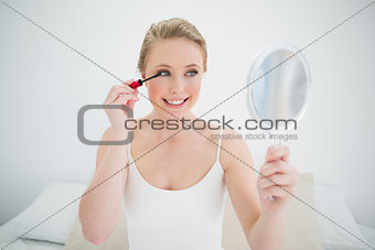 Natural cheerful blonde holding mirror and applying mascara
