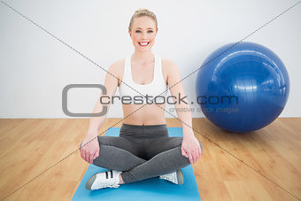 Smiling sporty blonde sitting cross legged on exercise mat