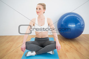 Content sporty blonde sitting cross legged on exercise mat