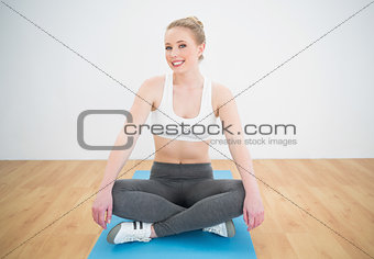 Gleeful sporty blonde sitting cross legged on exercise mat
