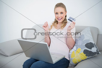 Casual thrilled blonde holding credit card and laptop