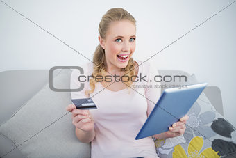 Casual thrilled blonde holding tablet and credit card