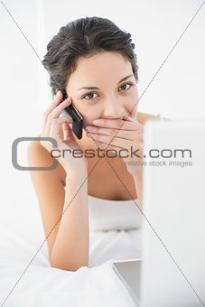 Shocked casual brunette in white pajamas making a phone call