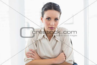 Stern stylish brunette businesswoman looking at camera and crossing her arms