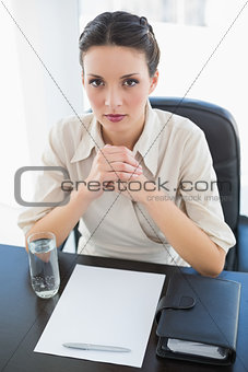 Stern stylish brunette businesswoman joining her hands and looking at camera