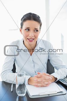 Skeptical stylish brunette businesswoman joining her hands and looking away