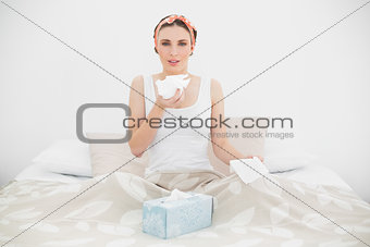 Sick woman holding a handkerchief sitting on her bed