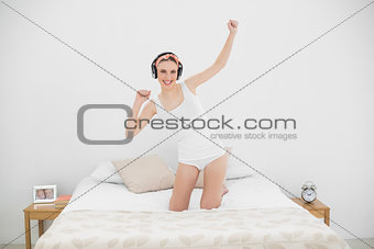 Young woman kneeling on her bed and listening to music