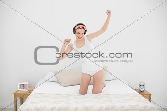 Young woman kneeling on her bed and moving while listening to music