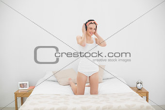 Smiling woman kneeling on her bed and wearing headphones