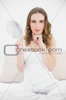 Pretty woman looking into the camera and holding a mirror