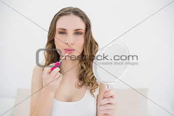 Young woman using lip gloss and looking into the camera