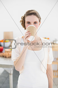 Cute woman standing in kitchen drinking of disposable cup