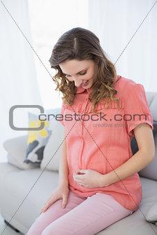 Cheerful pregnant woman sitting in the living room on a couch