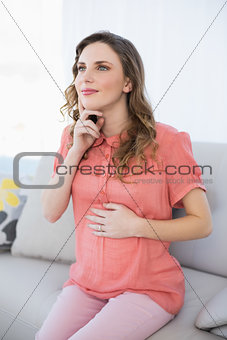 Thoughtful pregnant woman sitting on a couch in the living room