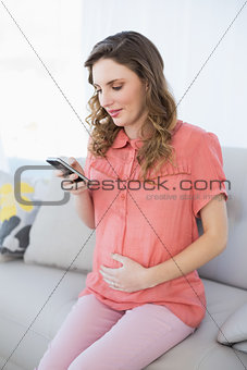 Calm pregnant woman using her smartphone sitting on a couch in the living room